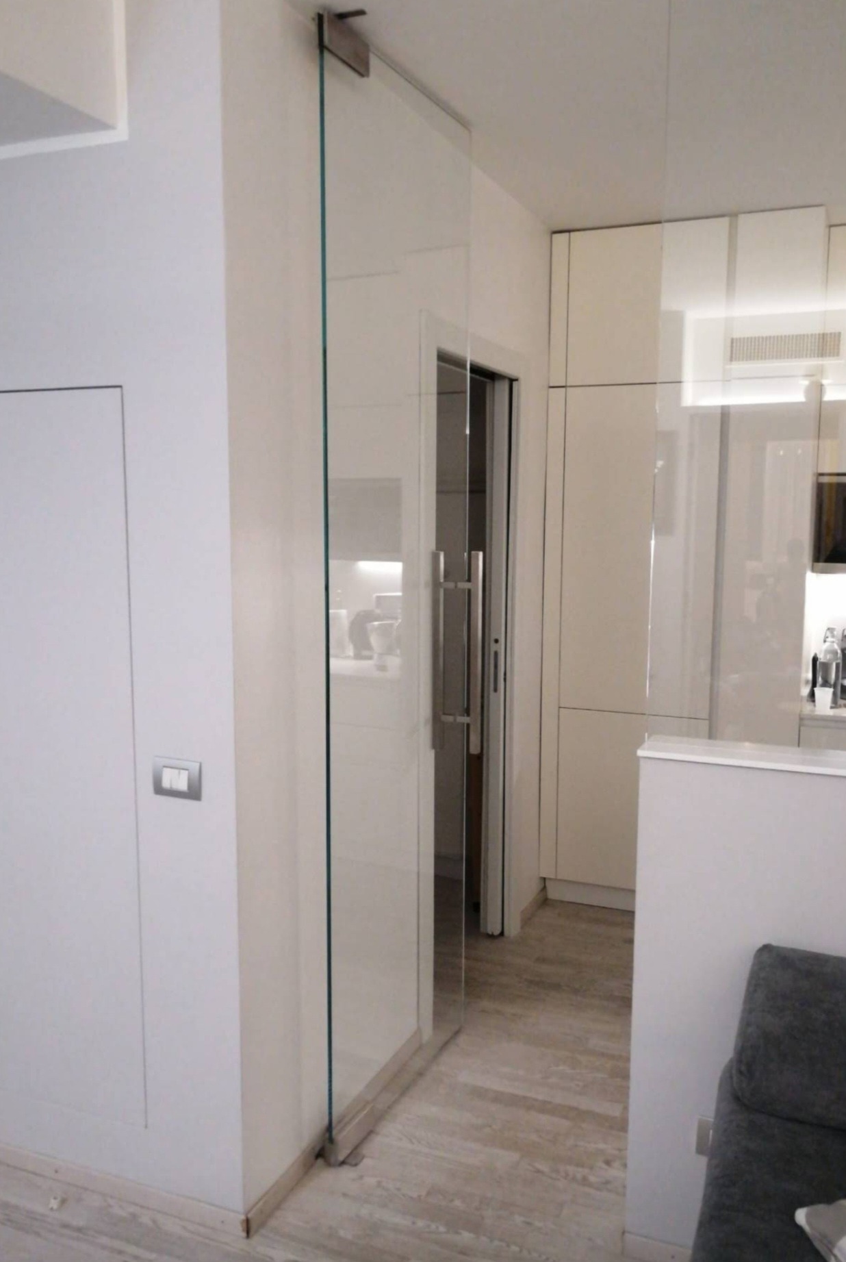 Nowoczesne, przesuwne drzwi szklane z metalowym uchwytem, zamontowane w białym wnętrzu. Widoczna minimalistyczna aranżacja kuchni w tle.