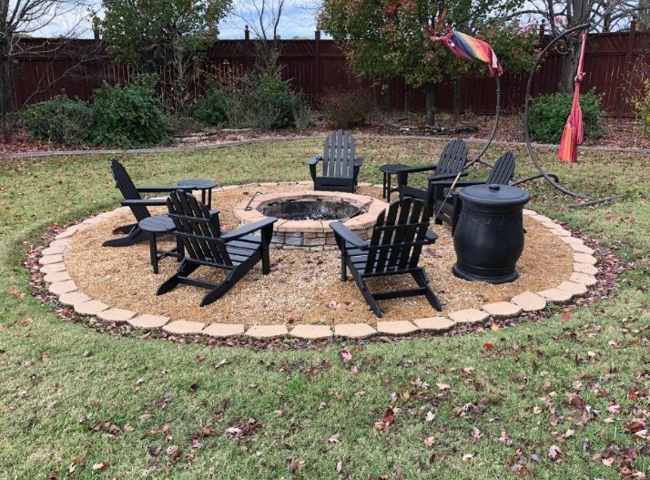 Ognisko otoczone kostką, żwirem i czarnymi krzesłami Adirondack w ogrodzie. W tle widoczny płot i drzewa. Elementy dekoracyjne, takie jak hamak, dodają uroku.