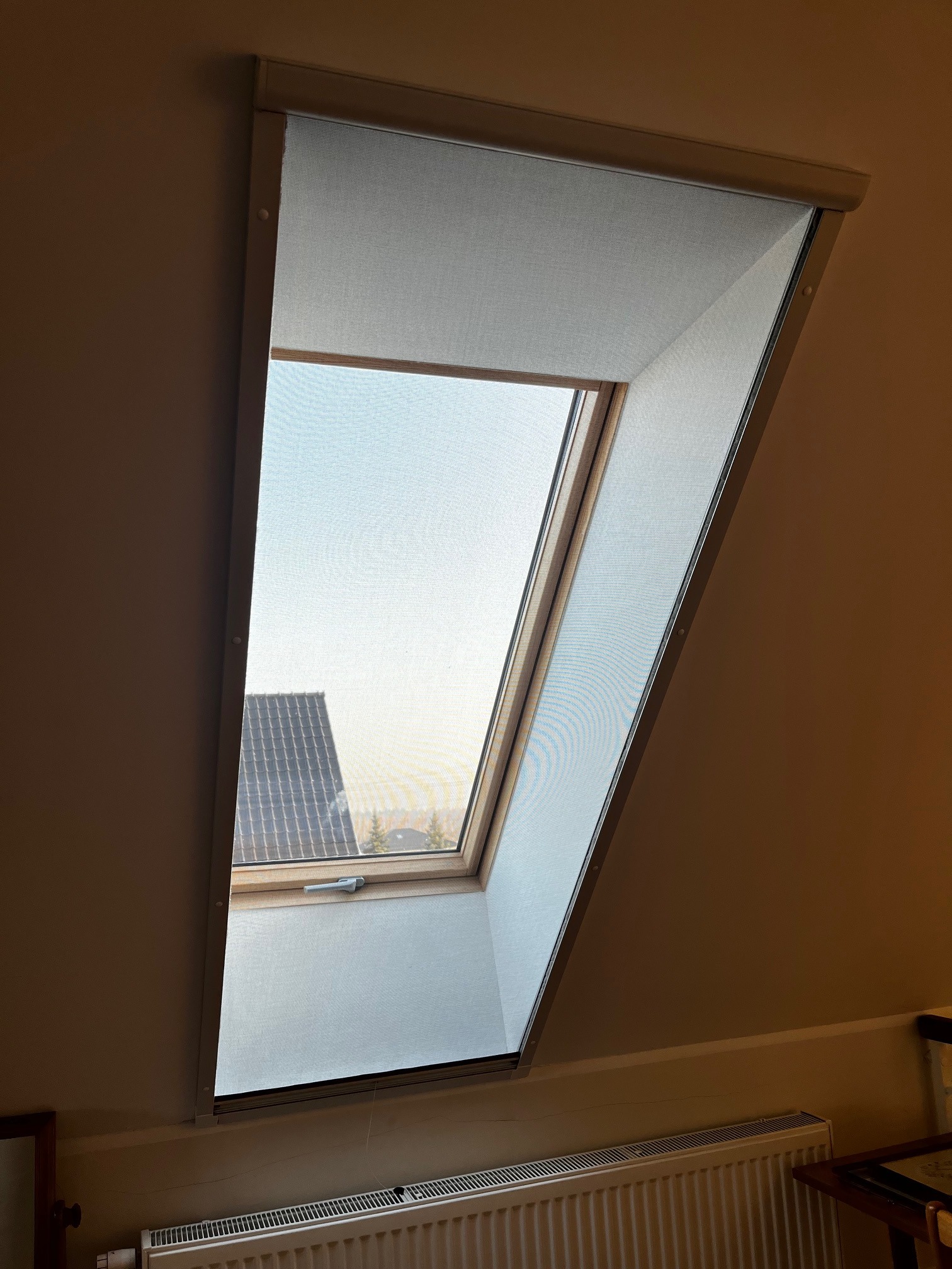 Zamknięta moskitiera w oknie dachowym, widok na dach budynku i niebo. Delikatna siatka moskitiery zapewnia ochronę przed owadami.