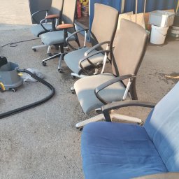 Norbert Ordon - Rząd krzeseł biurowych na kółkach, częściowo tapicerowanych, ustawionych na zewnątrz obok sprzętu czyszczącego, sugerujący przygotowanie do czyszczenia tapicerki.