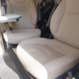 Norbert Ordon - Beżowe, tekstylne fotele kierowcy i pasażera w kamperze, widok z góry. Na podłodze szara wykładzina. Widoczna kierownica i stolik.