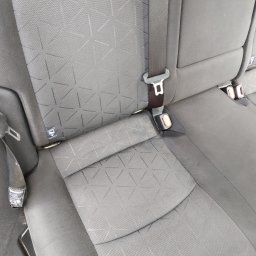 Norbert Ordon - Szare, tekstylne siedzenie samochodowe z pasami bezpieczeństwa. Widoczna faktura materiału i detale mocowań pasów. Czyste, zadbane wnętrze pojazdu.