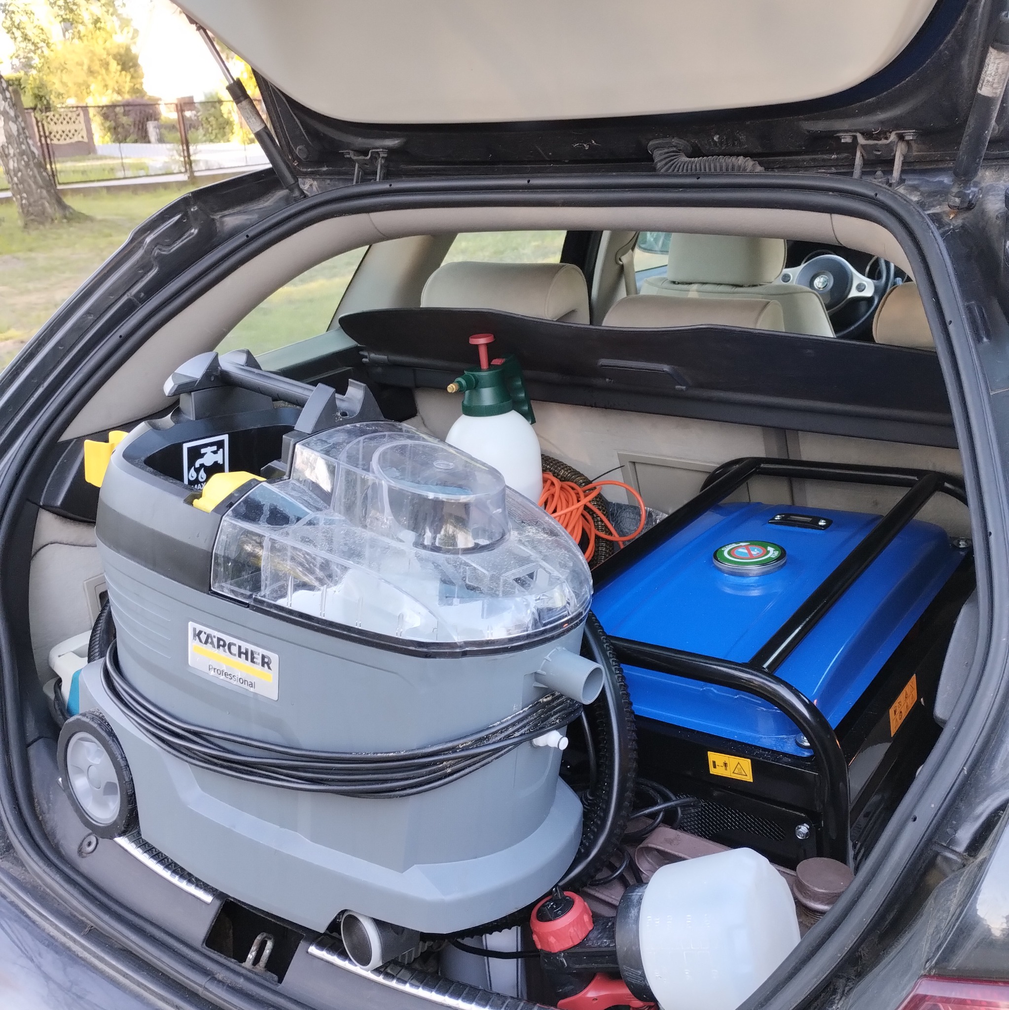 Sprzęt do prania tapicerki Karcher Professional i agregat prądotwórczy w bagażniku samochodu. Widok z zewnątrz, otwarty bagażnik.
