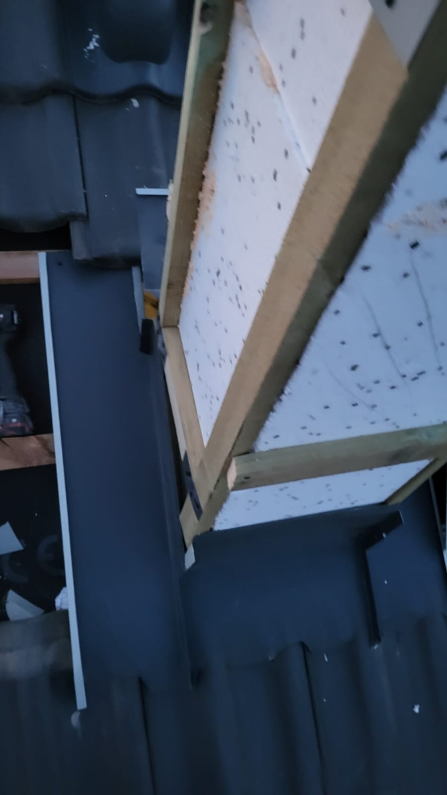 Montaż izolacji dachu z drewnianą ramą i czarną membraną dachową. Widok z góry, ukazujący detale konstrukcyjne i materiały użyte podczas prac dekarskich.