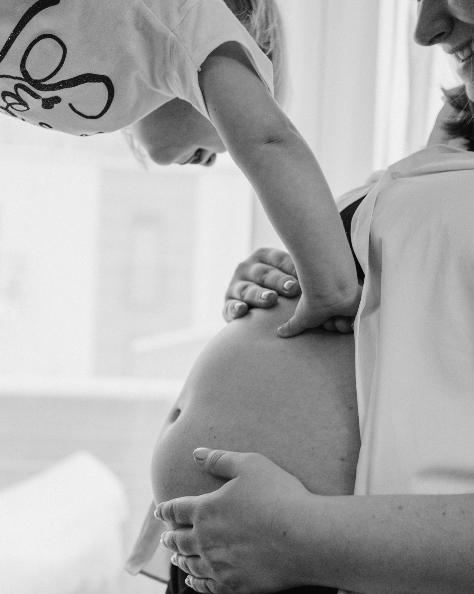 Czarno-białe zbliżenie na ciążowy brzuszek, na którym dziecko kładzie rączkę. Delikatne ujęcie z sesji ciążowej w Rybniku, podkreślające więź matki i dziecka.