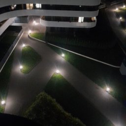 IGMAR - Nocny widok z góry na nowoczesny budynek z oświetlonymi ścieżkami i zielenią. Lampy wzdłuż chodników tworzą przyjemną atmosferę.