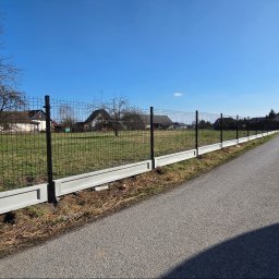 Redshop Wojciech Ustrzycki - Nowoczesne ogrodzenie panelowe z podmurówką betonową, widok z perspektywy ulicy, słoneczny dzień, błękitne niebo, domy w tle. Minimalistyczny design.