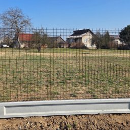 Redshop Wojciech Ustrzycki - Nowoczesne ogrodzenie panelowe z podmurówką betonową na tle domów jednorodzinnych i błękitnego nieba. Widok z bliska na fragment ogrodzenia.