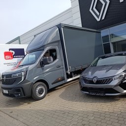 Dmytro Sveleba - Szary bus dostawczy z plandeką zaparkowany obok szarego samochodu osobowego na tle salonu Renault. Widoczny kierowca w kabinie.