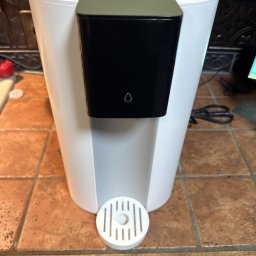 Mateusz Bajerski - Dystrybutor wody Waterdrop w białej obudowie z czarnym panelem, umieszczony na blacie z brązowych płytek. Widoczny fragment zmywarki.