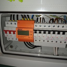 BILBO SPÓŁKA Z OGRANICZONĄ ODPOWIEDZIALNOŚCIĄ - Rozdzielnica elektryczna w obudowie, z widocznymi bezpiecznikami ETIMAT i pomarańczowym modułem SIMLIC LS-3F z wyświetlaczem. Widoczne przewody i elementy montażowe.