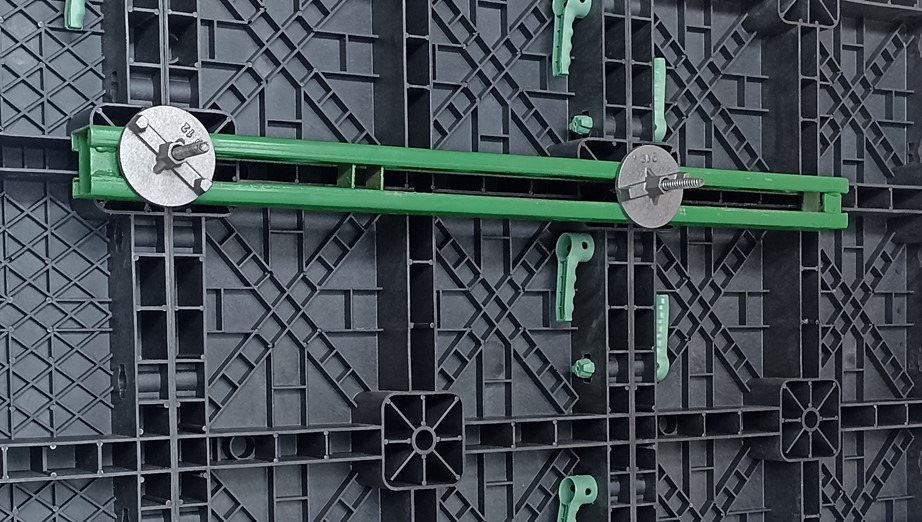 Szczegółowe ujęcie szalunku z tworzywa sztucznego z zielonym wzmocnieniem i metalowymi śrubami, ukazujące precyzję montażu i strukturę modułową.