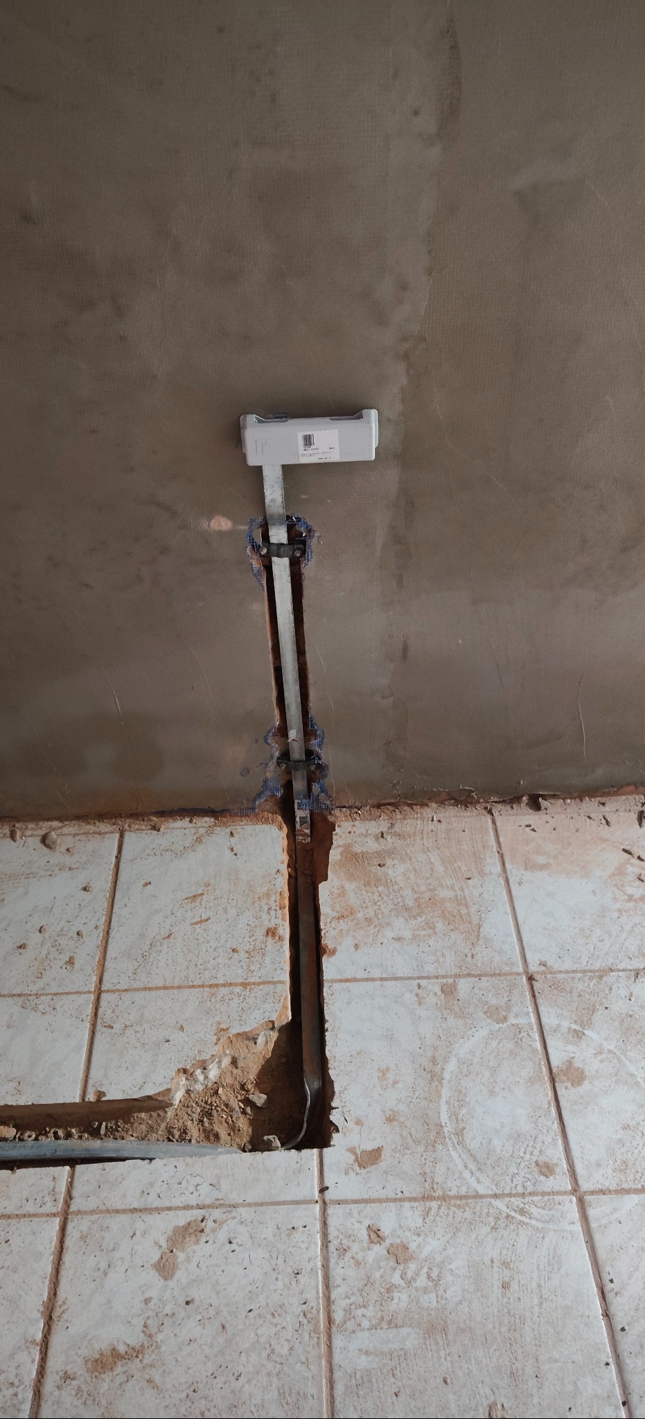 Bruzdowanie w ścianie i podłodze pod przewody. Widoczna puszka instalacyjna i metalowa listwa mocująca przewody. Uwidocznione kable w bruzdach.