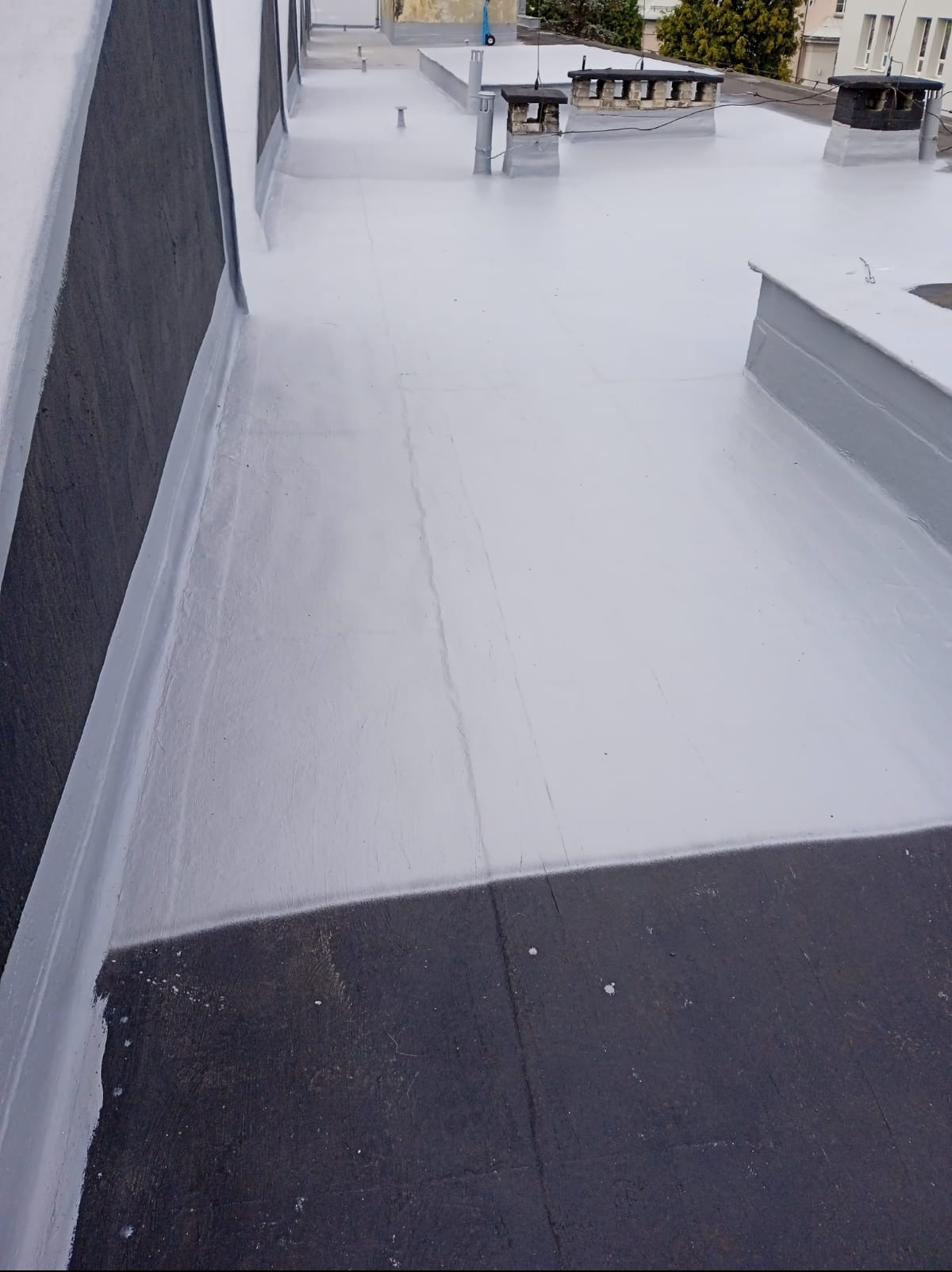 Jasnoszary, płaski dach po renowacji z widocznymi kominami i elementami wentylacyjnymi. Widok z góry, ukazujący gładką powierzchnię i detale wykończenia.