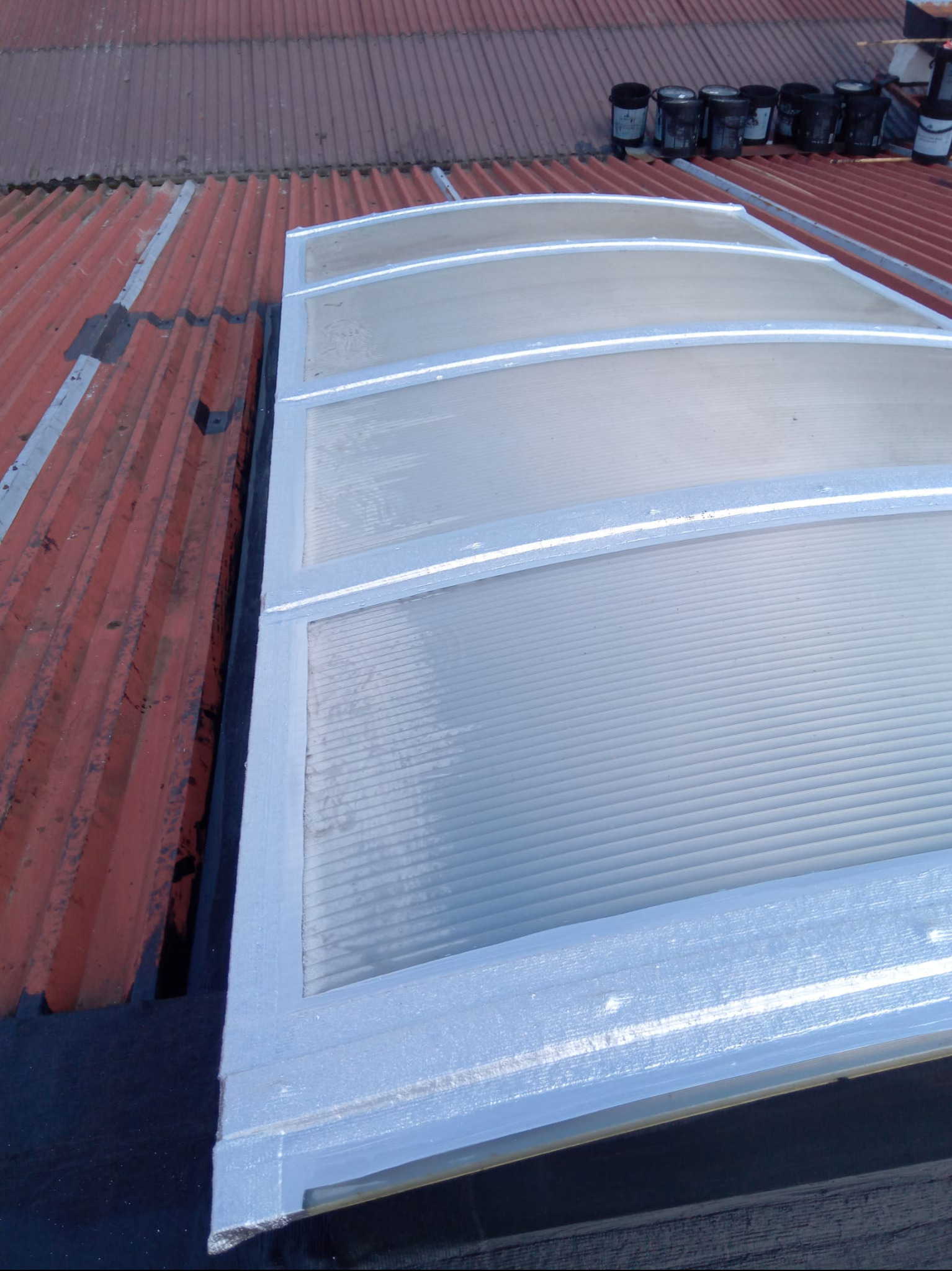 Zamontowany świetlik dachowy na dachu z blachy trapezowej, widoczne puszki z farbą. Detal wykończenia i uszczelnienia.