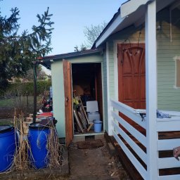 Mateusz Nowak - Otwarty, zagracony domek narzędziowy z niebieskimi beczkami na deszczówkę i świeżo pomalowaną werandą w ogrodzie. Widoczne narzędzia i akcesoria ogrodowe.