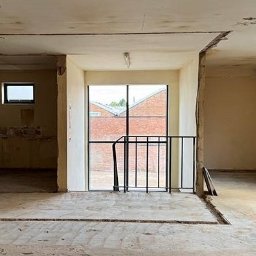 Wyburzenia Mazowieckie Mateusz Zalewski - Wnętrze po wyburzeniu ścian działowych, widoczne ślady po instalacjach w podłodze i suficie, okno z widokiem na ceglany budynek. Prace rozbiórkowe w trakcie.