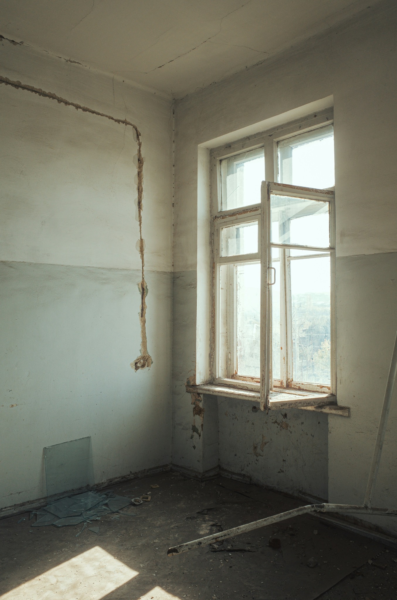 Wnętrze pokoju w trakcie rozbiórki: odsłonięte przewody na ścianie, otwarte okno, gruz na podłodze. Widoczne ślady po usuniętych elementach.