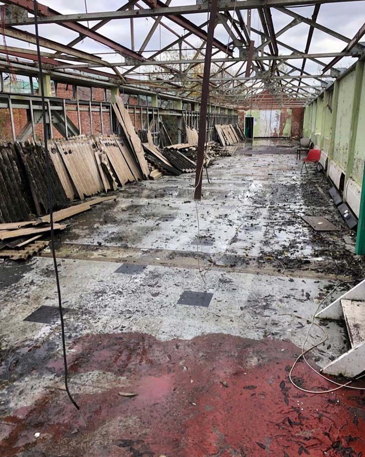 Wnętrze hali po rozbiórce: odsłonięta konstrukcja dachu, porozrzucane elementy, mokra podłoga z resztkami materiałów. Widoczny czerwony fotel i fragmenty ścian.