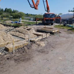 Piotr Zasadny Budownictwo - Wylewanie betonu do wykopów pod fundamenty domu jednorodzinnego. Na drugim planie betoniarka i pompa do betonu.