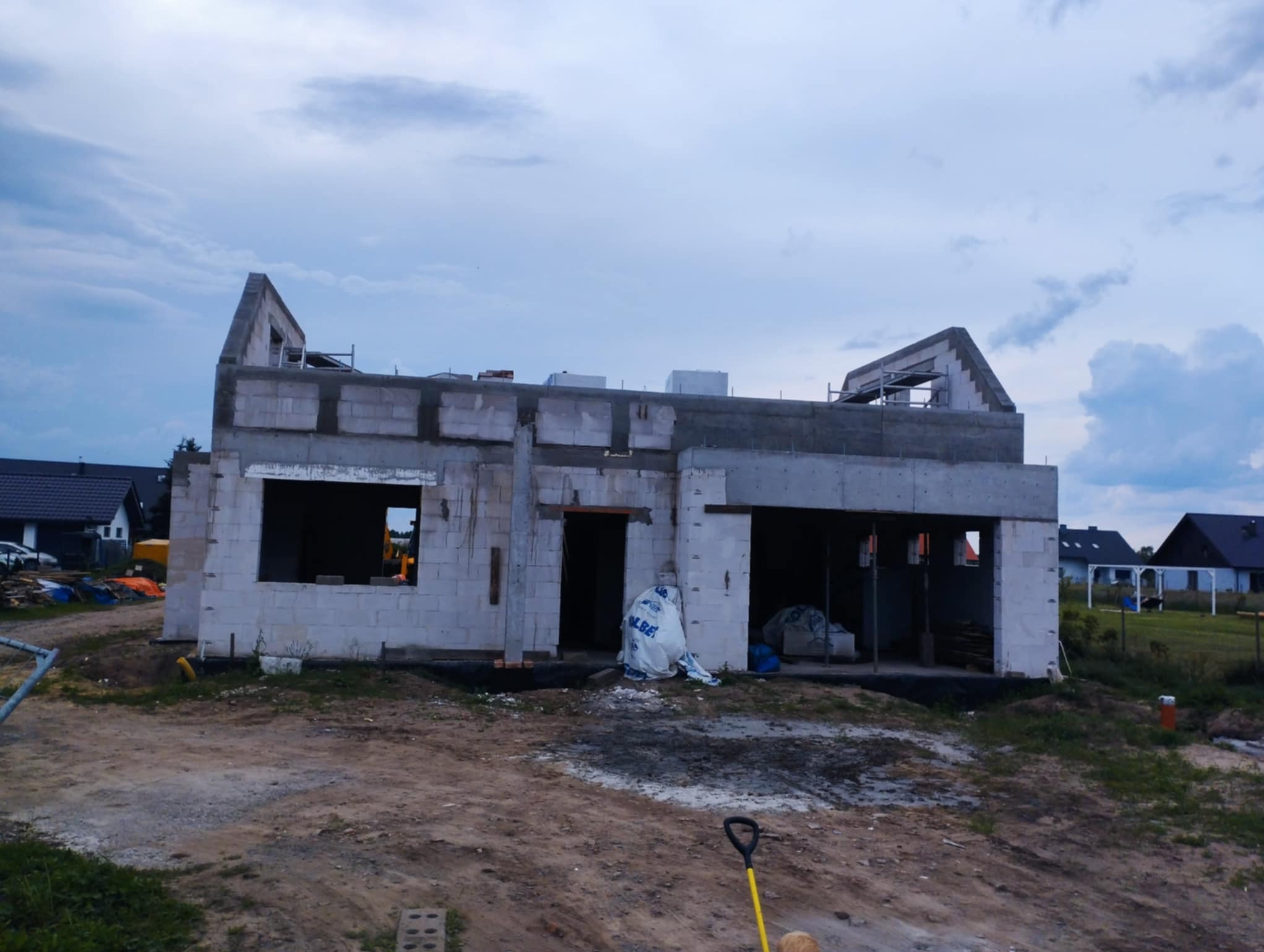 Budowa domu jednorodzinnego w stanie surowym otwartym z betonu komórkowego. Widoczne ściany, otwory okienne i drzwiowe, oraz częściowo wykonany strop.