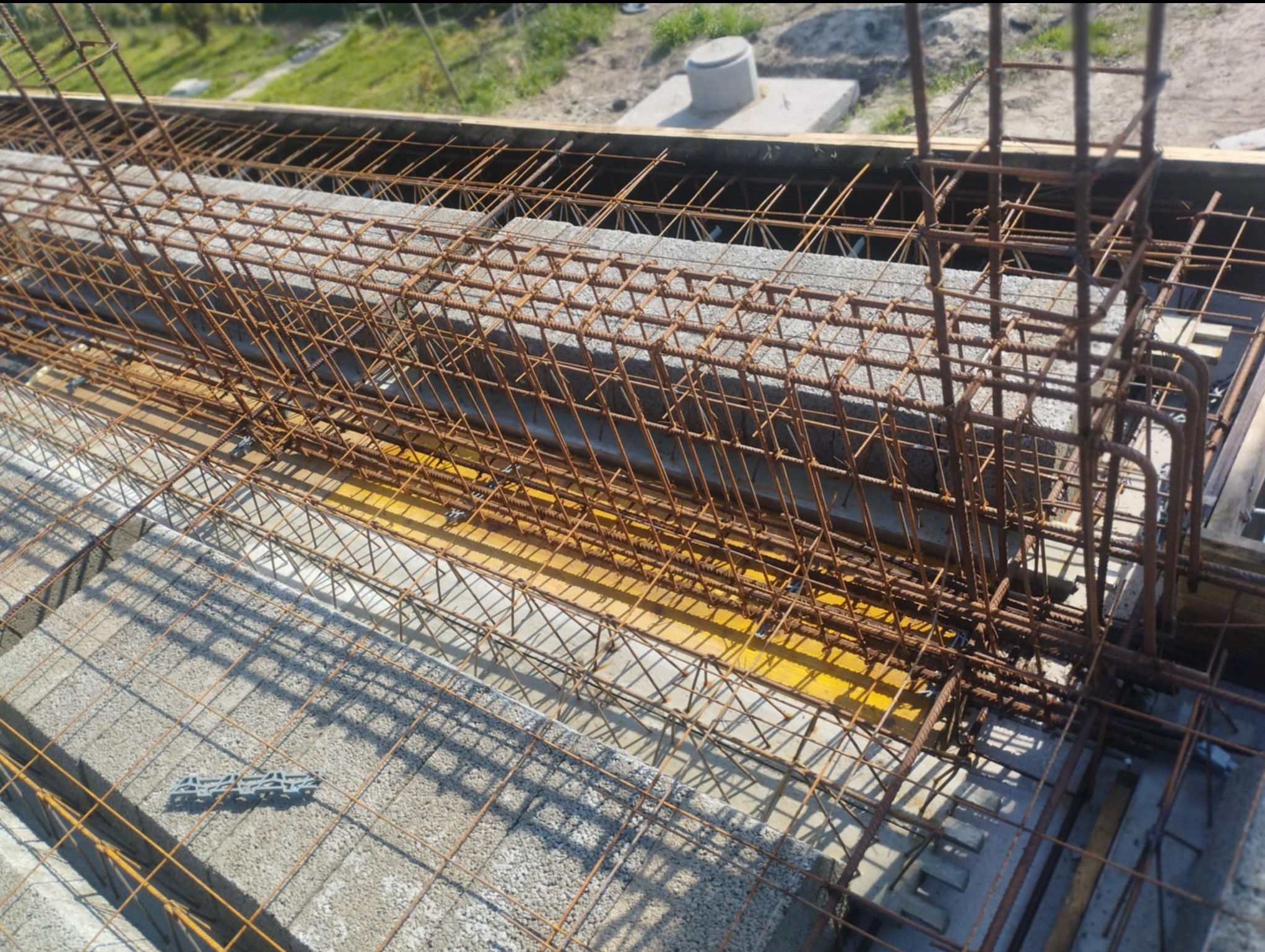 Zbrojenie stropu z betonu komórkowego Ytong, widok z góry. Stalowe pręty tworzą siatkę, przygotowaną do zalania betonem. Żółte elementy szalunku widoczne w tle.