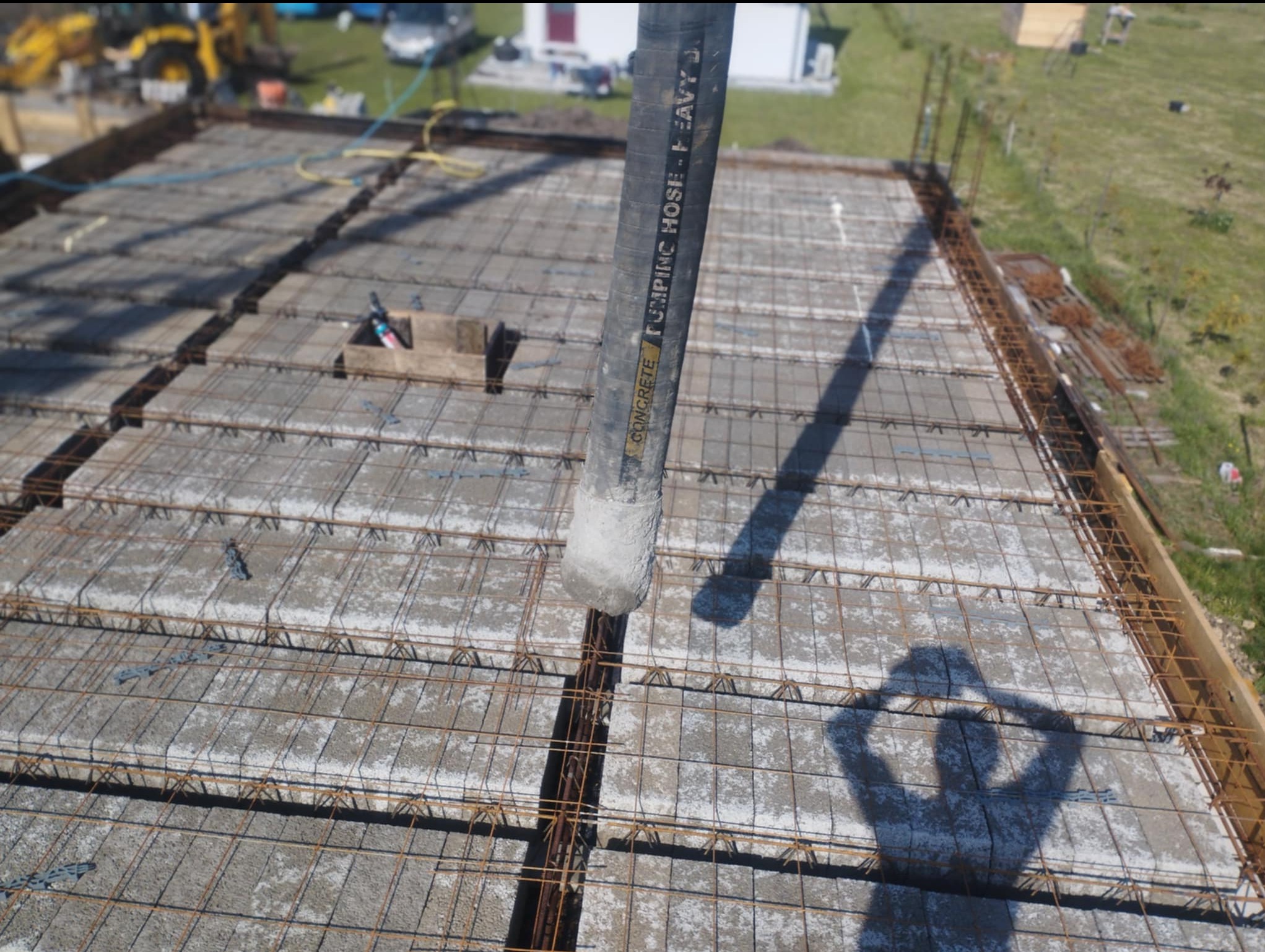 Wylewanie betonu na strop Teriva zbrojony siatką stalową. Widoczny wąż do pompowania betonu i cień osoby obsługującej pompę. Prace budowlane w toku.