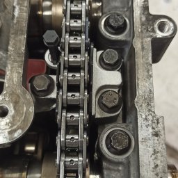 NorthTruck Norbert Kiczor - Otwarty silnik samochodowy z widocznym łańcuchem rozrządu, śrubami i elementami metalowymi. Szczegółowe ujęcie mechanizmu w trakcie naprawy lub serwisu.