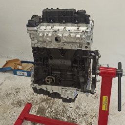 NorthTruck Norbert Kiczor - Silnik samochodowy po regeneracji, zawieszony na czerwonym stojaku w warsztacie. Widoczne świeżo pomalowane elementy i czysty blok silnika.