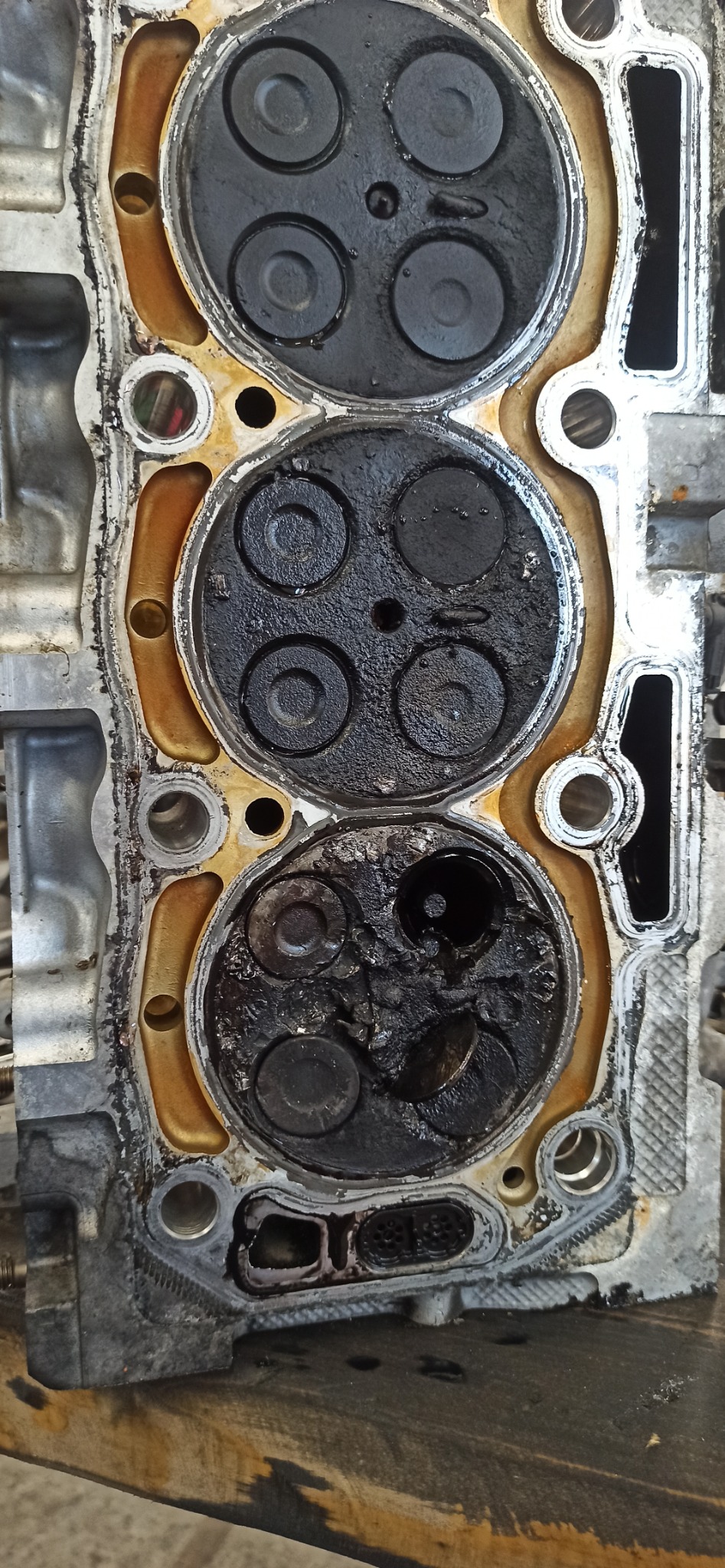 Głowica silnika spalinowego z widocznymi nagarami na zaworach, ukazująca zużycie i potrzebę naprawy. Detaliczny widok na wnętrze silnika.