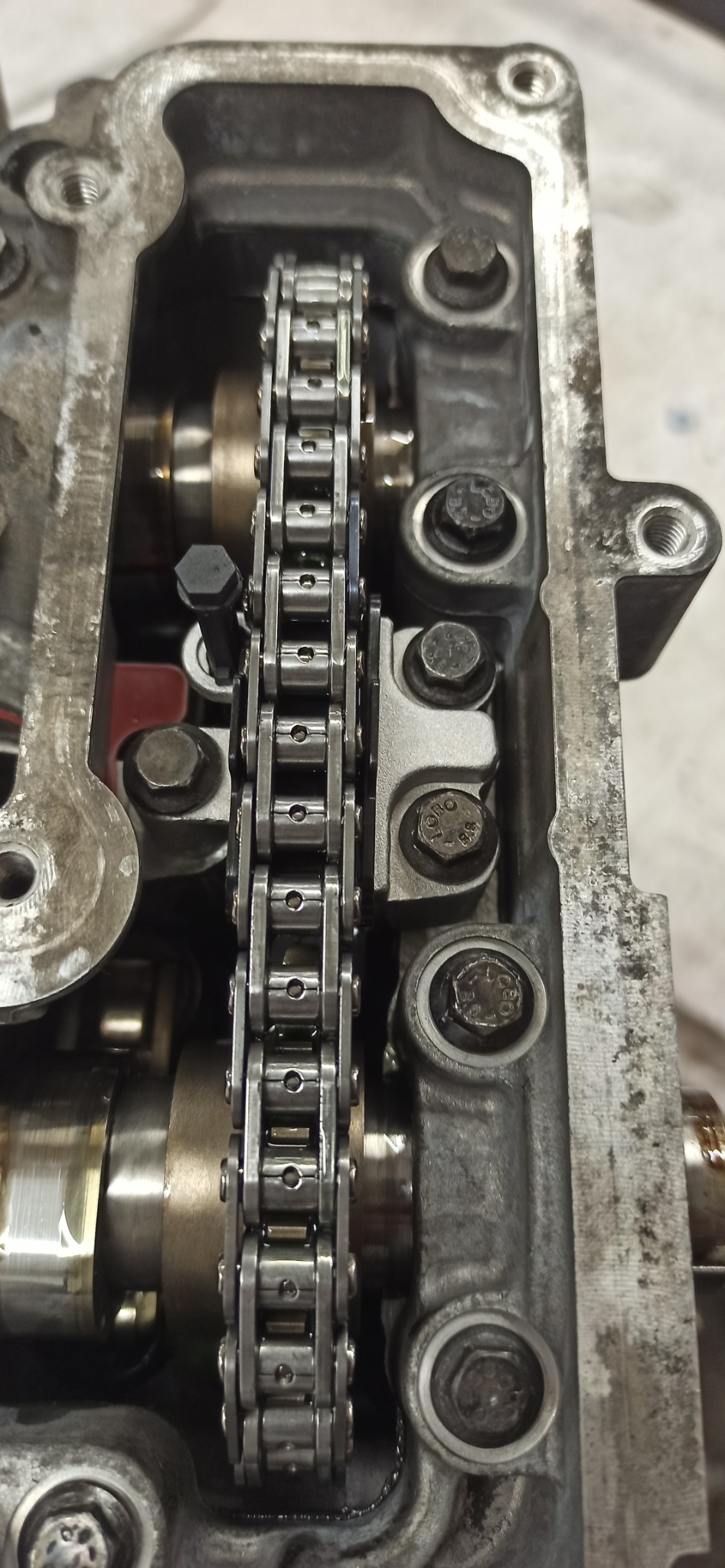 Otwarty silnik samochodowy z widocznym łańcuchem rozrządu, śrubami i elementami metalowymi. Szczegółowe ujęcie mechanizmu w trakcie naprawy lub serwisu.