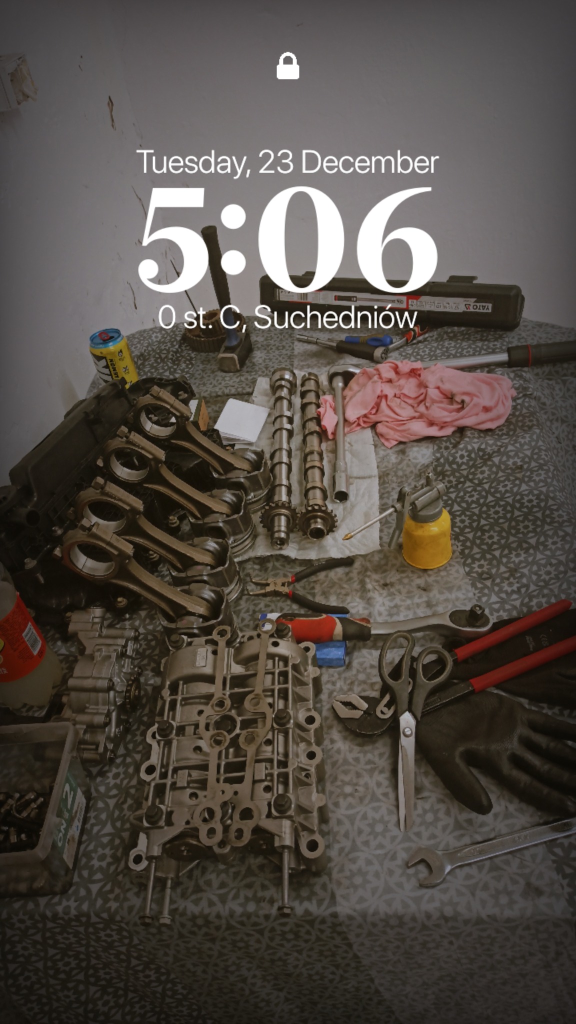 Rozłożony silnik samochodowy z narzędziami na wzorzystej tkaninie. Widoczne wałki rozrządu, korbowody, blok silnika i akcesoria warsztatowe.