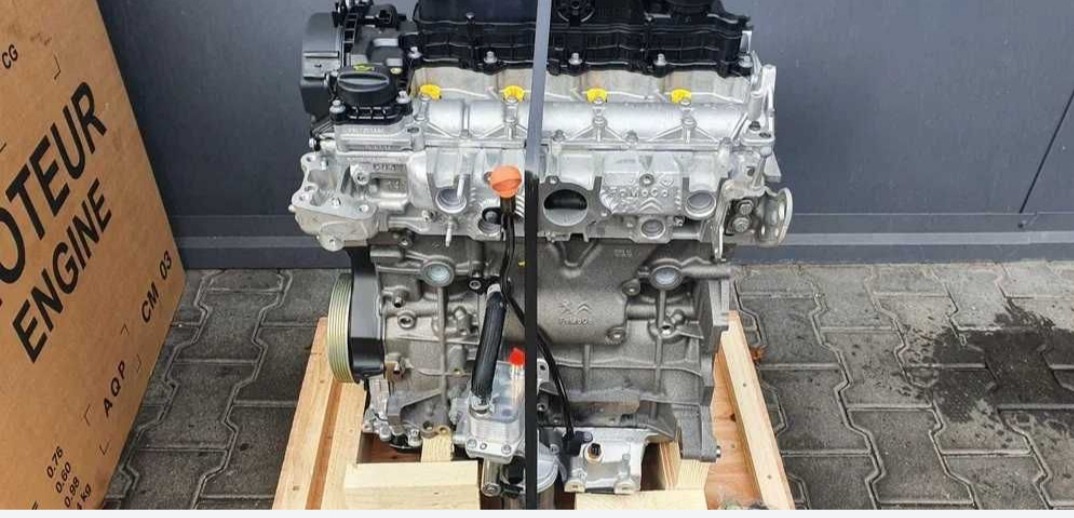 Silnik samochodowy na drewnianej palecie, widok z przodu, z widocznymi detalami konstrukcyjnymi i oznaczeniami producenta. Obok karton z napisem 'Moteur Engine'.