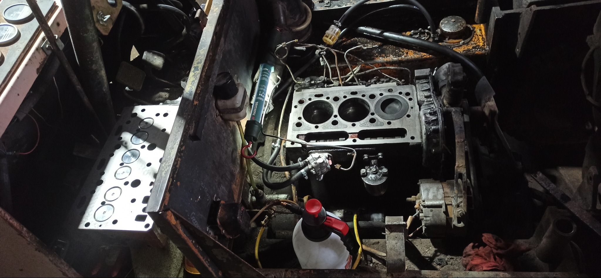 Silnik rozebrany do naprawy, widoczna głowica cylindrów, narzędzia i oświetlenie warsztatowe. Detal mechaniczny w trakcie serwisu.