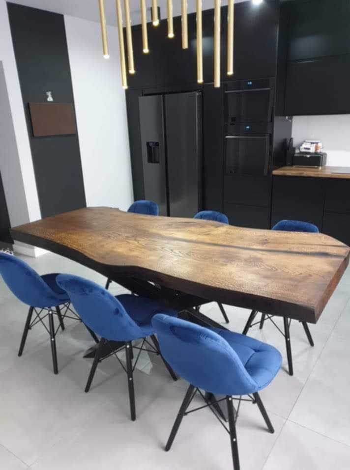 Stół z litego drewna o nieregularnych krawędziach w nowoczesnej jadalni z czarnymi meblami i niebieskimi krzesłami. Unikalny design i oświetlenie.