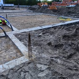 Oleksii Levytskyi - Fundamenty domu w trakcie budowy, z widocznymi zbrojeniami, betonowymi bloczkami i sprzętem budowlanym w tle, w słoneczny dzień.