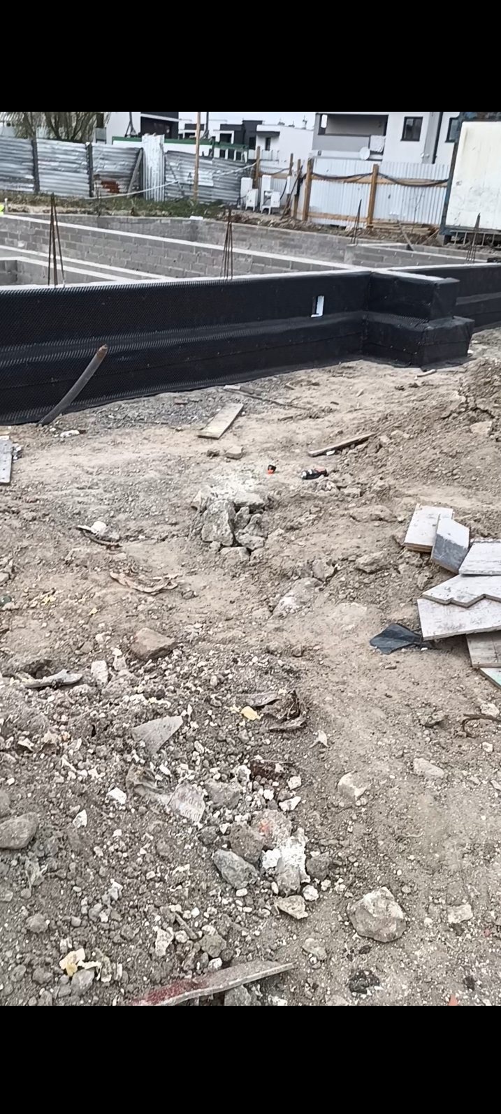 Fundamenty domu z izolacją przeciwwilgociową, widoczne bloczki betonowe i teren budowy. Ujęcie z bliska, podkreślające detale izolacji.