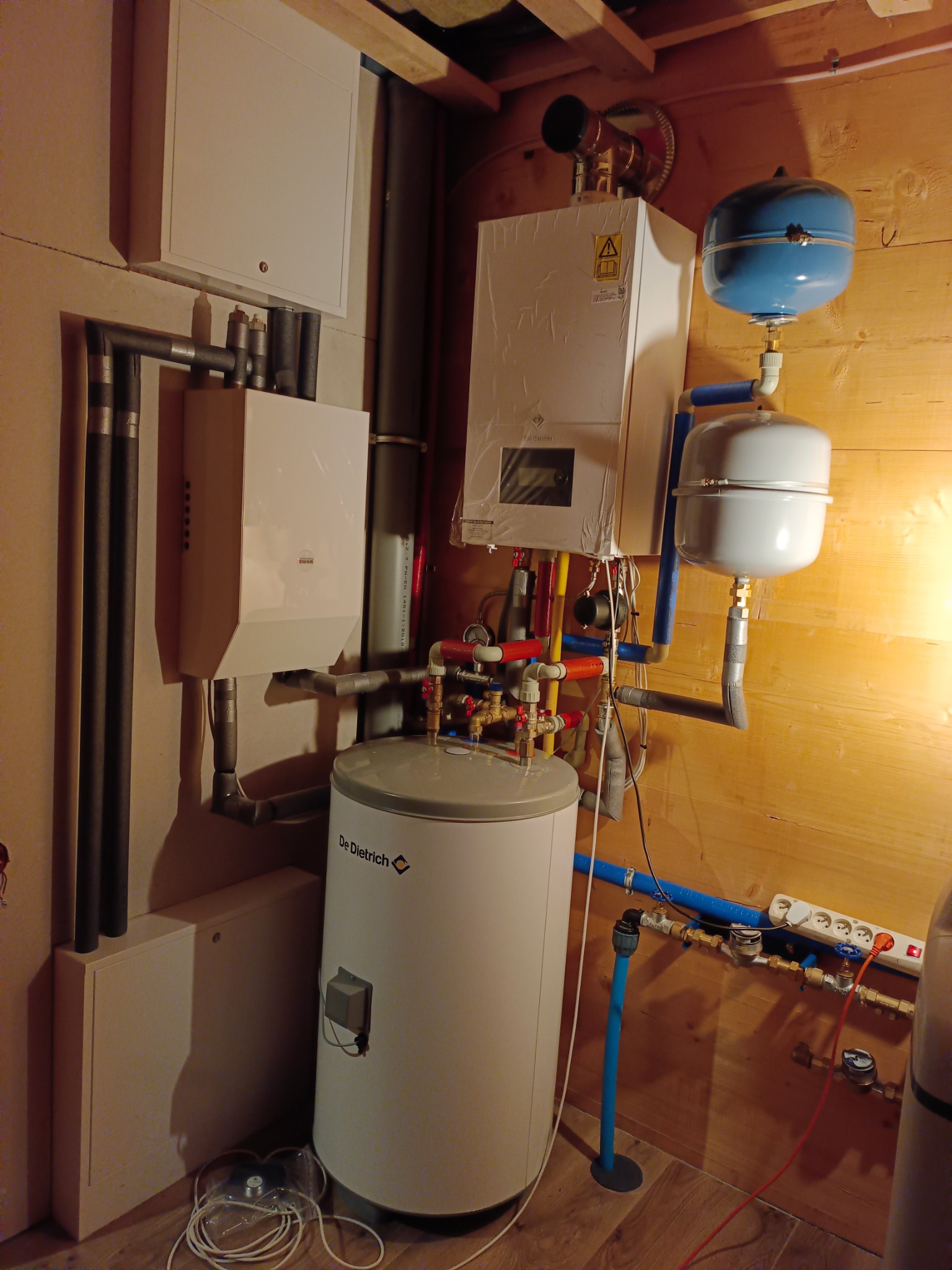 Kompleksowa instalacja grzewcza z piecem gazowym, zbiornikiem i rurami w kotłowni wykończonej drewnem. Widoczne elementy armatury i zabezpieczenia.