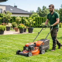 Maciej and - Mężczyzna kosiarką Husqvarna dba o trawnik w ogrodzie w Krakowie. Widoczne drzewa i krzewy w donicach. Usługa koszenia trawy.