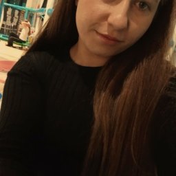 Magdalena Kobus - Portret kobiety z długimi brązowymi włosami w czarnym swetrze, na tle sali zabaw dla dzieci z niebieskimi elementami konstrukcyjnymi.