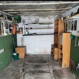 Pusto pl - Zagracony garaż z drewnianą podłogą, regałami, drabiną i różnymi przedmiotami na półkach. Ściany pomalowane na zielono i biało, sufit przykryty folią.