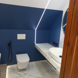 USŁUGI REMONTOWO-BUDOWLANE MYKHAILO HAIDUK - Niebieska łazienka na poddaszu z marmurową posadzką i blatem, oświetleniem LED wzdłuż ściany i nowoczesną armaturą. Umywalka owalna, toaleta podwieszana.