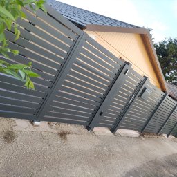 Iron Tech Solutions - Nowoczesne, poziome ogrodzenie panelowe w kolorze grafitowym, z widoczną furtką i fragmentem domu w tle. Ujęcie z poziomu gruntu, podkreślające linię ogrodzenia.