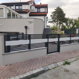 Iron Tech Solutions - Nowoczesne ogrodzenie panelowe z poziomymi, czarnymi przęsłami i mlecznym szkłem, osadzone na niskim, szarym murku. W tle dom z przeszkloną werandą i czerwonym dachem.