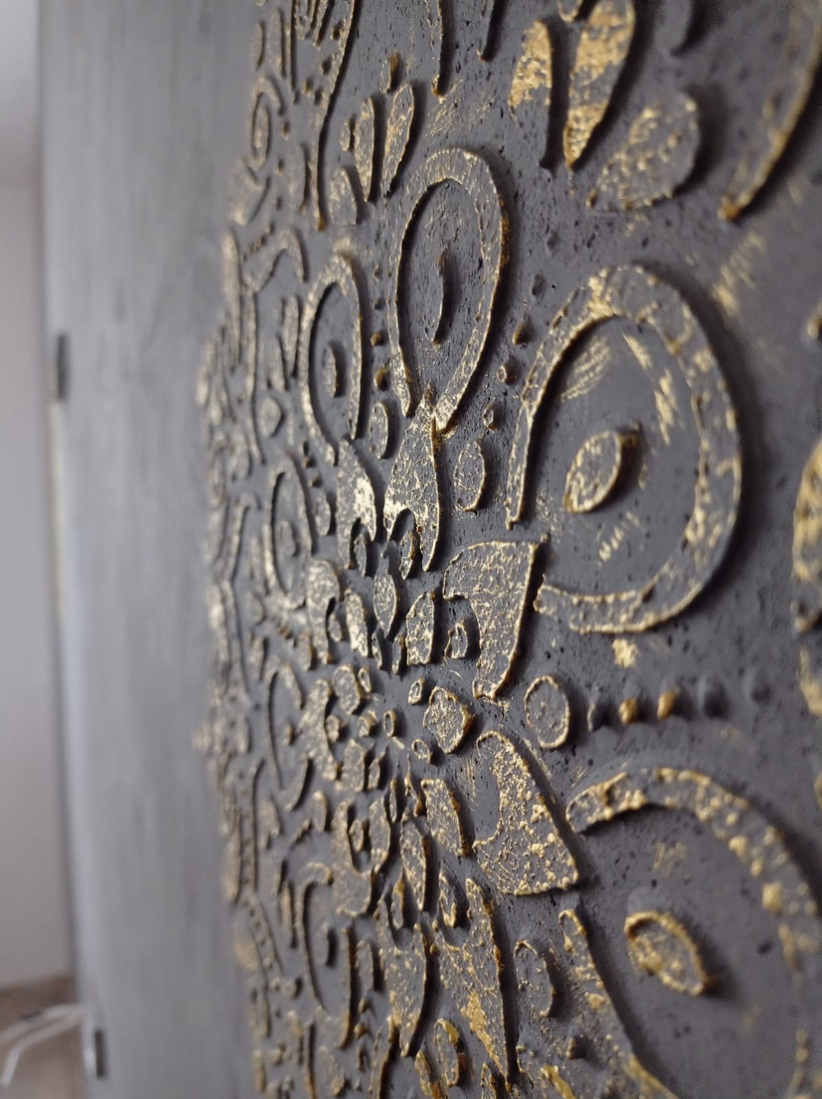 Dekoracyjna ściana z efektem strukturalnym w odcieniach szarości i złota, z bliska, ukazująca detale wzoru. Unikalna faktura i gra światła podkreślają artystyczny charakter.