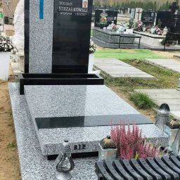 GALAN PRZEMYSŁAW ŁUKASZEWSKI - Granitowy nagrobek z niebieskim krzyżem na cmentarzu, z inskrypcją i zdjęciem zmarłego, otoczony kwiatami i lampionami, na tle innych grobów i drzew.