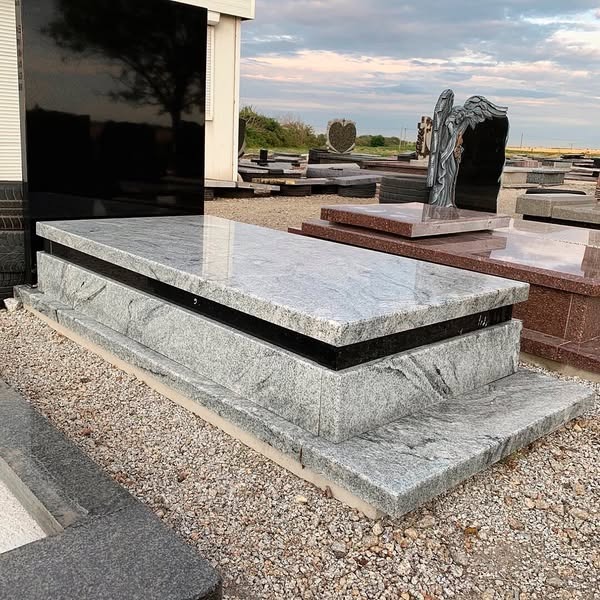 Granitowy nagrobek z czarnym akcentem, widoczny na ekspozycji wśród innych nagrobków. Szary kamień z wyraźnym wzorem, prosta forma.