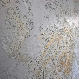 ARTESSA HOME SPÓŁKA Z OGRANICZONĄ ODPOWIEDZIALNOŚCIĄ - Dekoracyjna ściana z szarego tynku strukturalnego z ornamentem w stylu mandali, wykończonym złotą farbą. Efektowna faktura i unikalny wzór.