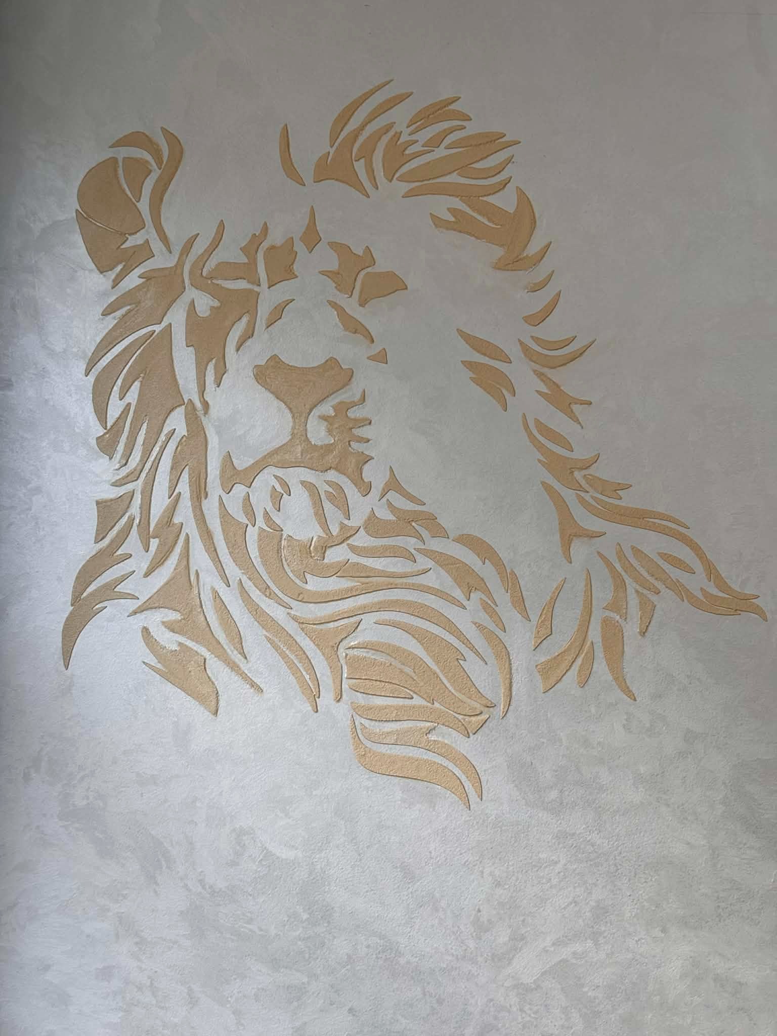 Dekoracyjna ściana z efektem stiuku w odcieniach szarości, na której widnieje złoty, abstrakcyjny wizerunek lwa. Unikalna faktura i gra świateł dodają wnętrzu elegancji.