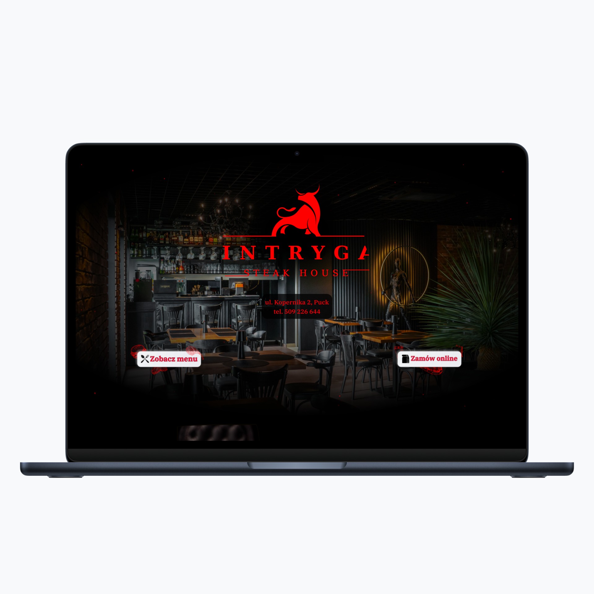 Laptop wyświetla stronę internetową restauracji Intryga Steak House z Pucka, z widocznym wnętrzem, logo czerwonego byka i przyciskami menu oraz zamówień online.